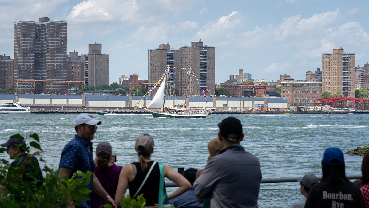 New Yorkers watch as the Liberty Clipper sails along the East River during a preliminary parade on July 3, 2026, in the Brooklyn borough of New York City.