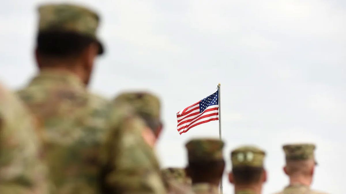 An image of US Army soldiers walking behind a U.S. flag.