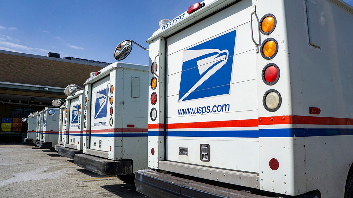 Row of USPS delivery trucks parked in a lot.