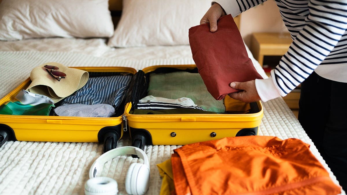 Woman packs a suitcase on a bed in a home setting.