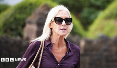 A woman with blonde hair is wearing a purple shirt and sunglasses and hoop earrings.