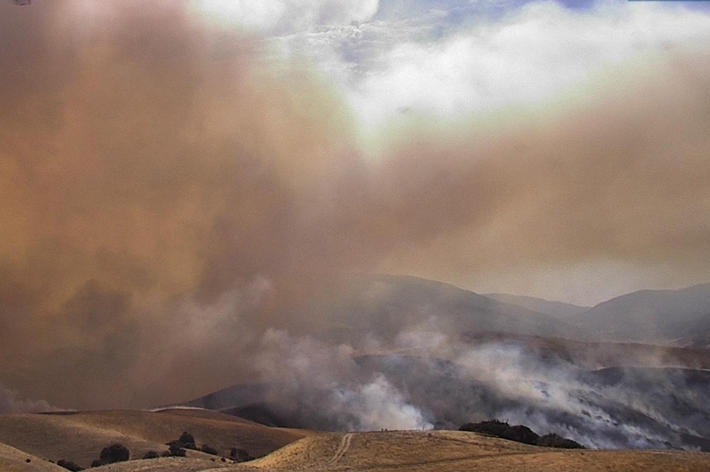 Wildfire smoke rising from hills into a hazy sky.