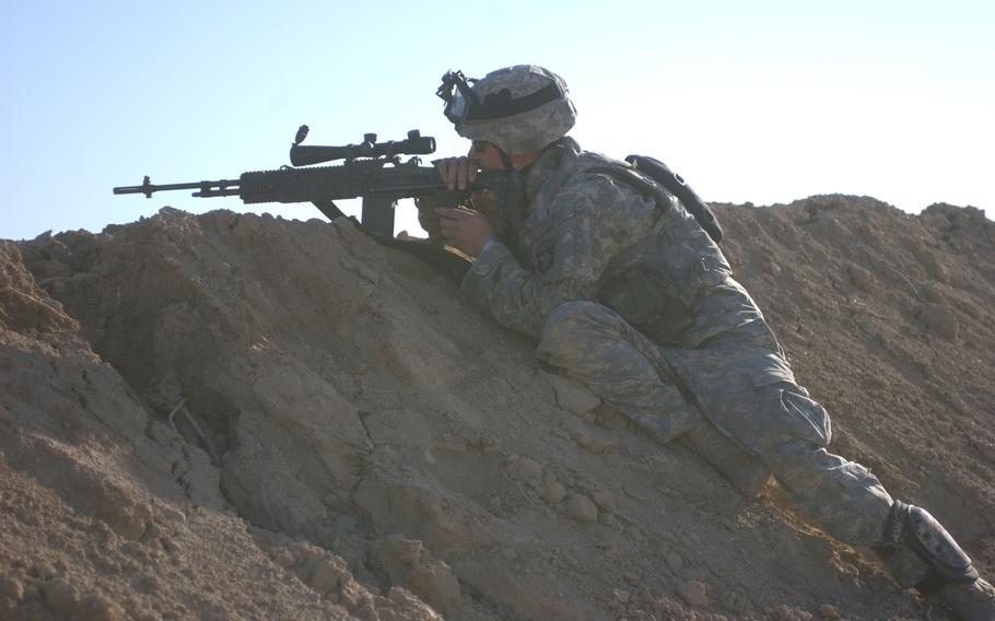 A soldier lies on a rock and looks through the scope of his rifle.