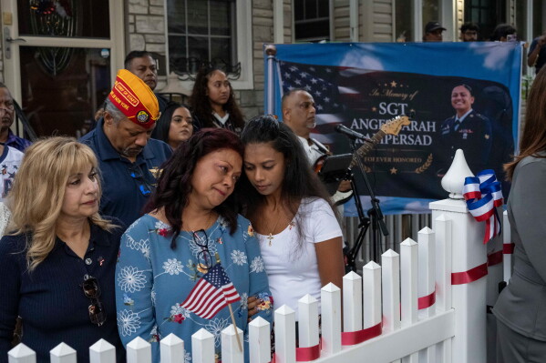 Family of Sgt. Angel Sarah Rampersad, aunt Judy Rackal, left, mother Carol Acevedo, center, and sister Laura Tamby, right, attend a candlelight vigil outside her home in Ozone Park, Monday, July 27, 2026, in the Queens borough of New York. (AP Photo/Yuki Iwamura)
