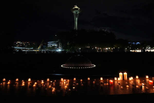 With a backdrop of the Space Needle, candles are seen lighted during the vigil for victims the day after a shooting at Seattle Center during the Bite of Seattle food festival, Monday, July 27, 2026, in Seattle. (AP Photo/Lindsey Wasson)