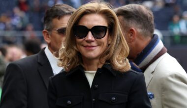 Smiling woman with blonde hair and black sunglasses in a black coat
