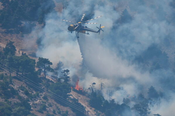 A firefighting helicopter drops water over a wildfire on Mount Kithairon near Porto Germeno, northwest of Athens, Greece, Monday, Aug. 3, 2026. (AP Photo/Petros Giannakouris)