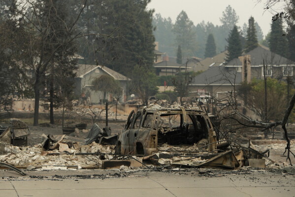 A vehicle and structure are burned on N. Skyline Dr. due to a wildfire, Sunday, Aug. 2, 2026, in Spokane, Wash. (AP Photo/Young Kwak)