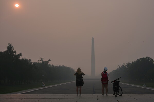 The sun is obscured by wildfire smoke as people stop to photograph the Washington Monument and Lincoln Memorial Reflecting Pool, July 17, 2026, on the National Mall in Washington. (AP Photo/Julia Demaree Nikhinson, File)