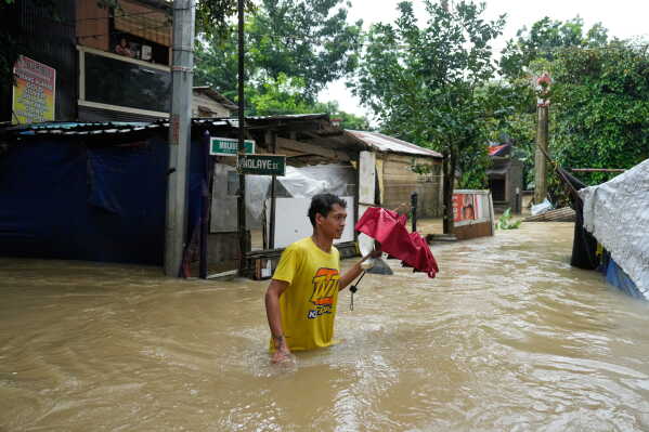 A man walks through floodwaters caused by heavy seasonal monsoon rains at Bagong Silangan village in Quezon city, Metro Manila, Philippines Monday, Aug. 10, 2026. (AP Photo/Aaron Favila) CORRECTION: Corrects typo in location to Silangan, instead of Silagan