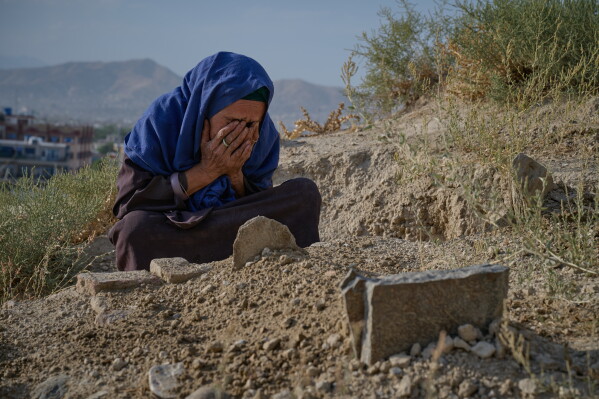 Sima covers her face at the grave of her six-month-old granddaughter, her daughter Diba's daughter, who died during the winter, in Kabul, Afghanistan, Wednesday, Aug. 12, 2026. Originally from Mazar-e-Sharif in northern Afghanistan, Sima, who believes she is about 60 but does not know her exact age, helps support her extended family by begging and collecting items she can reuse or sell. (AP Photo/Nava Jamshidi)