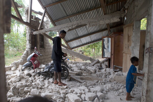 Saverinus Serli, left, inspects his earthquake-damaged house in Lelak, East Nusa Tenggara province, Indonesia, Sunday, Aug. 16, 2026. (AP Photo/Firdia Lisnawati)
