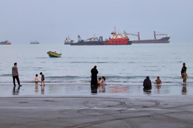 People spend time at a beach as commercial vessels are anchored in the Strait of Hormuz.