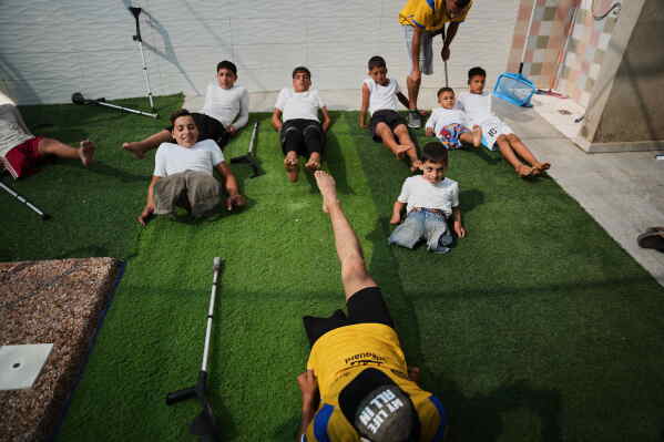 Coach Nour Qashqash warms up with children who lost their legs after being injured in the war between Israel and Hamas during a swimming training session organized by the Heal Palestine organization at a pool in Khan Younis, Gaza Strip, Wednesday, Aug. 19, 2026. (AP Photo/Abdel Kareem Hana)