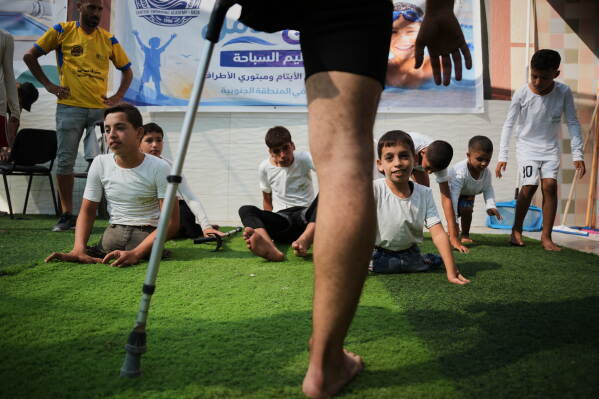 Coach Nour Qashqash warms up with children who lost limbs after being injured during the war between Israel and Hamas, during a swimming training session organized by the Heal Palestine organization at a pool in Khan Younis, Gaza Strip, Wednesday, Aug. 19, 2026. (AP Photo/Abdel Kareem Hana)