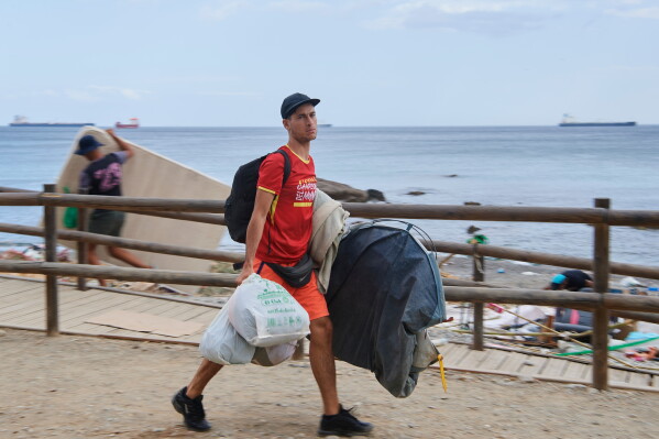 A migrant who crossed from Morocco into Spain gathers his belongings after being cleared from the beach in the Spanish exclave of Ceuta, Thursday, Aug. 20, 2026. (AP Photo/Antonio Sempere)