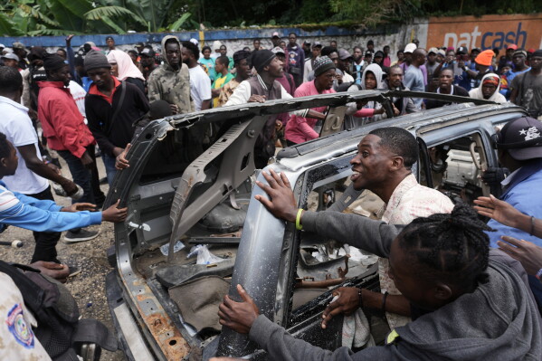 Residents try to flip over a car to block a street as they protest for police intervention after deadly gang attacks in the Kenscoff neighborhood of Port-au-Prince, Haiti, Monday, Aug. 24, 2026. (AP Photo/Odelyn Joseph)