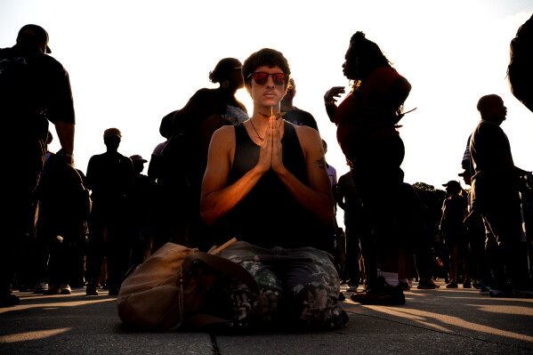 A demonstrator holds a paper crane while kneeling in front of the Lincoln Memorial before the March on Washington, Friday, Aug. 28, 2026, in Washington. (AP Photo/Julia Demaree Nikhinson)