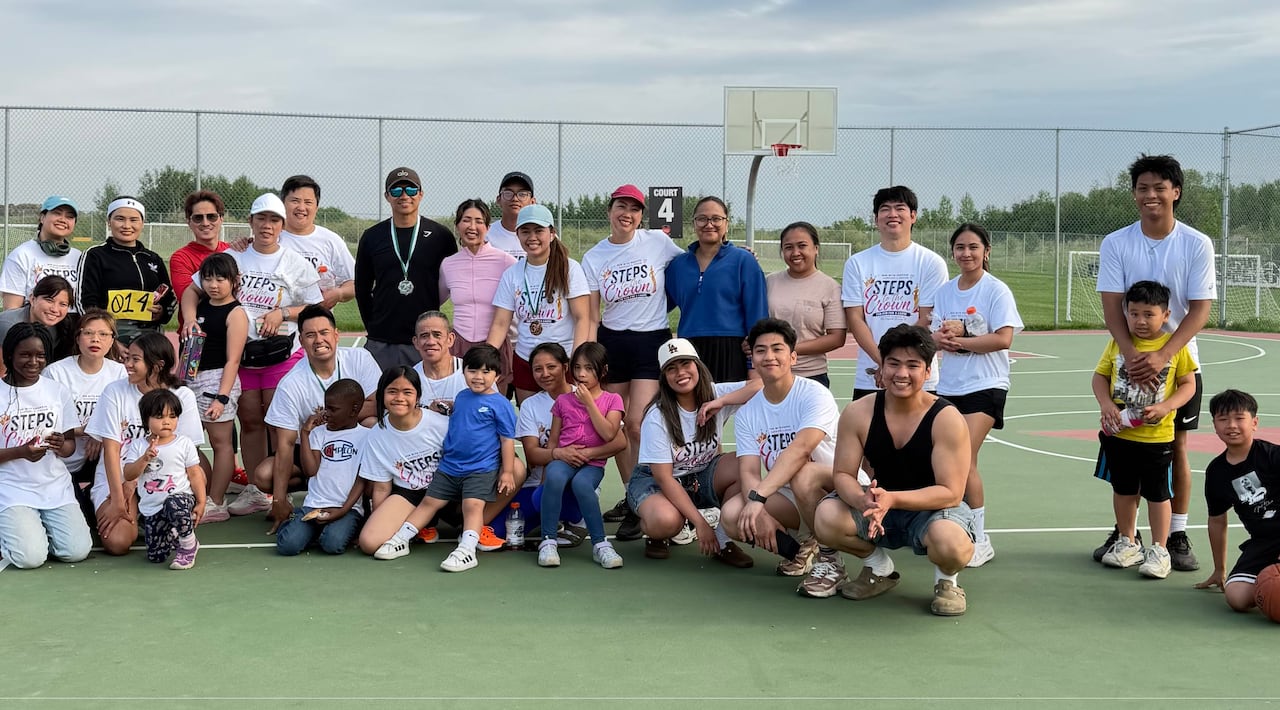 A large group of people in sportswear pose for a photo on an outdoor basketball court.