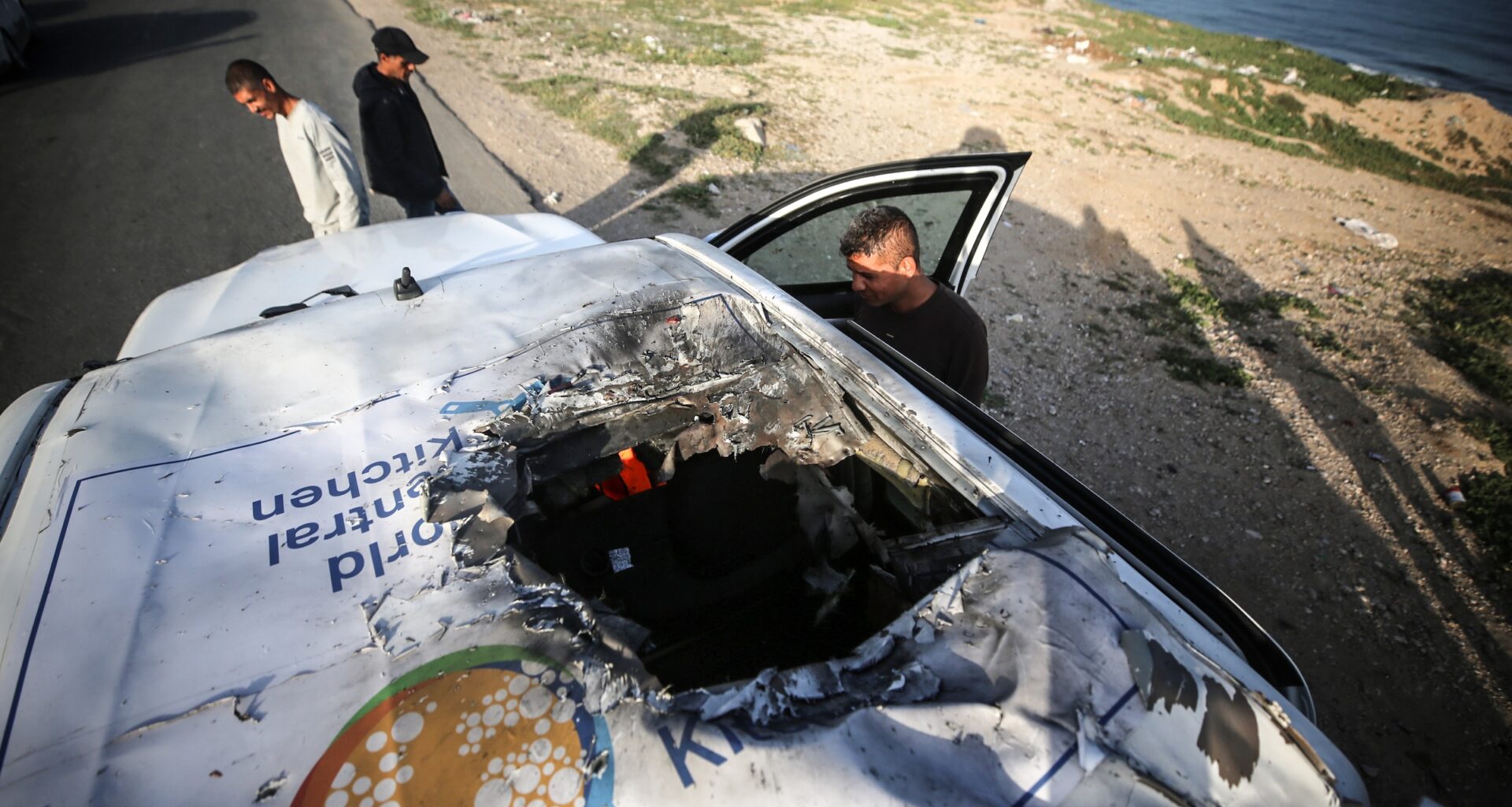Palestinians are standing next to a vehicle in Deir Al-Balah, in the central Gaza Strip, on April 2, 2024, where employees from the World Central Kitchen (WCK), including foreigners, were killed in an Israeli airstrike.