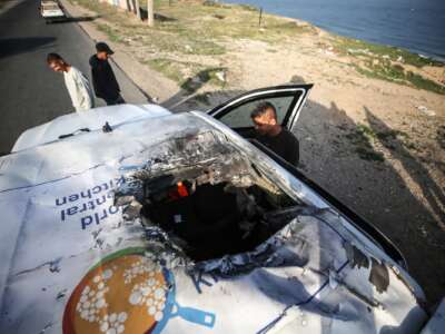 Palestinians are standing next to a vehicle in Deir Al-Balah, in the central Gaza Strip, on April 2, 2024, where employees from the World Central Kitchen (WCK), including foreigners, were killed in an Israeli airstrike.
