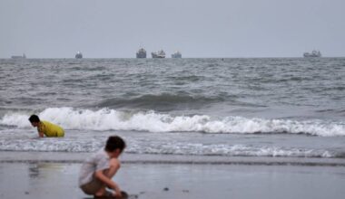 Children play at a beach as commercial vessels are anchored in the Strait of Hormuz off Bandar ...
