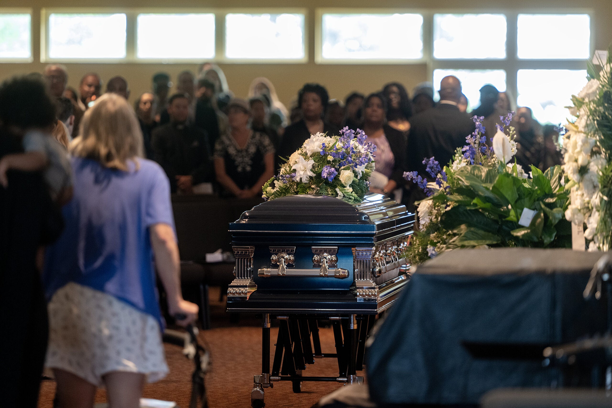 A casket adorned with flowers sits in a church filled with mourners during a funeral service.