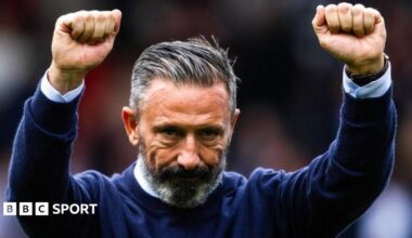 Derek McInnes, in a dark blue jumper, raises both arms in celebration