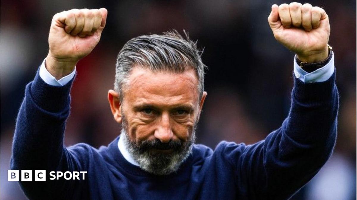 Derek McInnes, in a dark blue jumper, raises both arms in celebration
