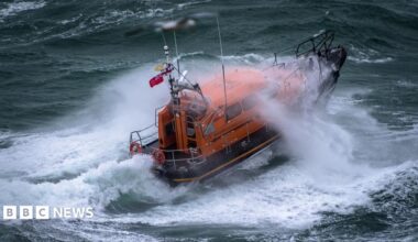 A Shannon class lifeboat in rough swell with a wave breaking over it.