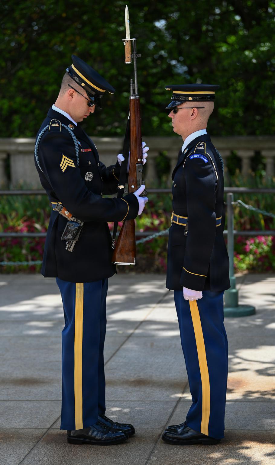 One guard inspects the rifle as the other stands at attention.