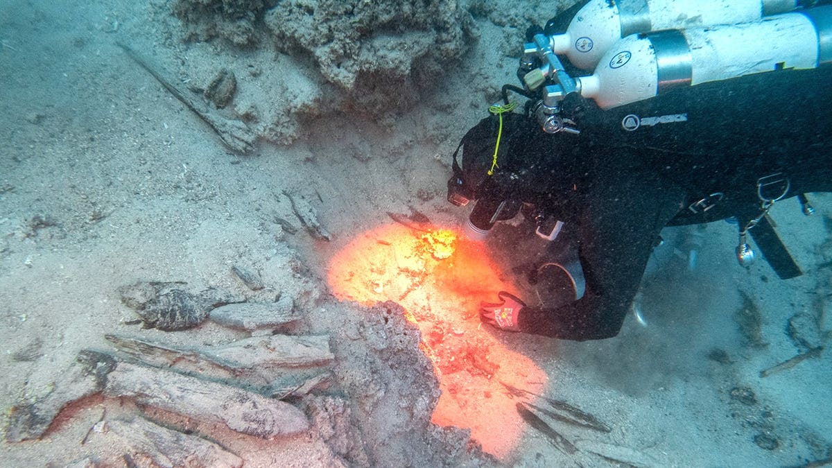 Diver analyzing shipwreck underwater with orange light