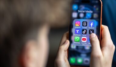 a 14-year-old boy holds an iPhone screen displaying various social media and messaging apps