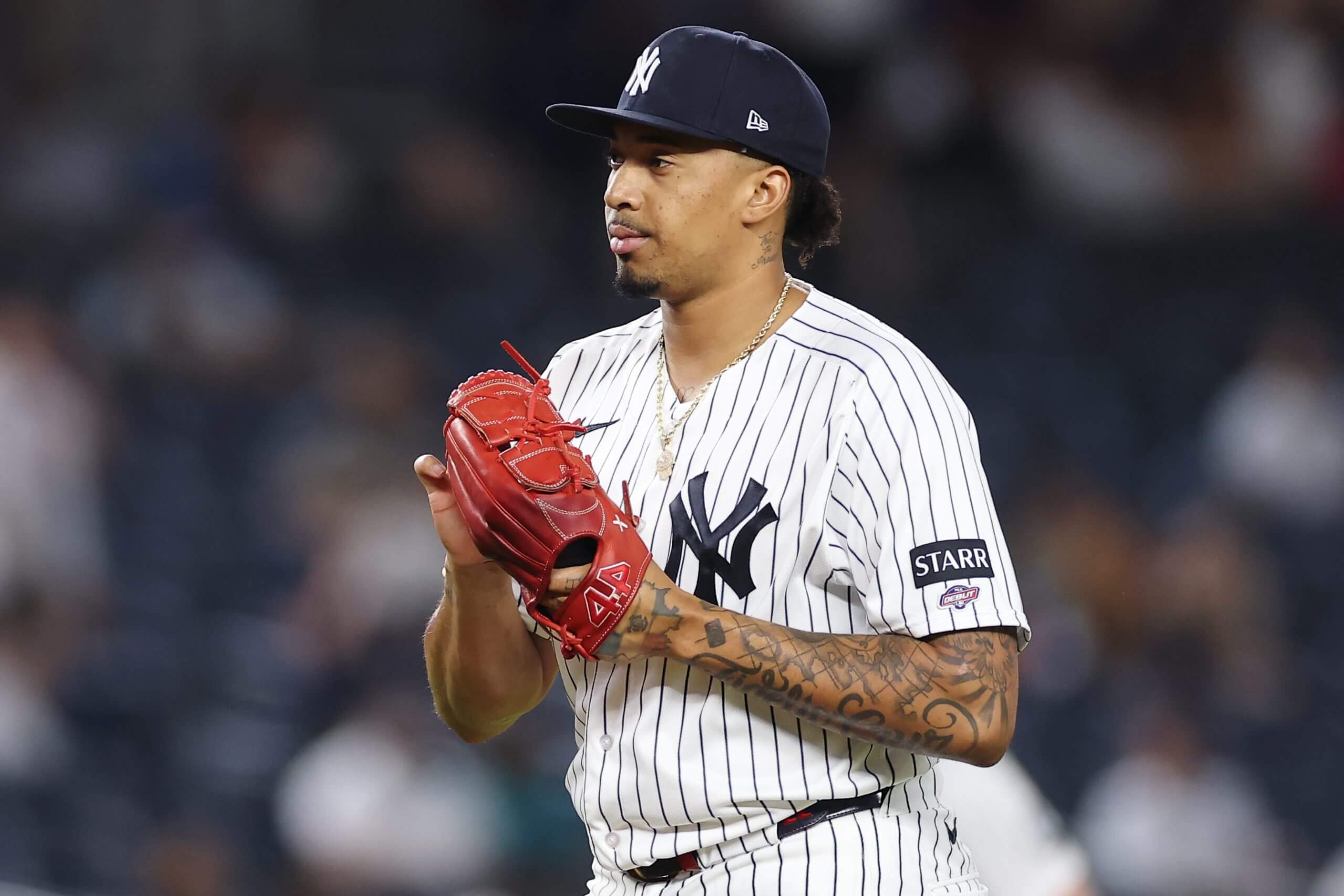 Yovanny Cruz of the New York Yankees smiles slightly while holding his red baseball glove after making his MLB debut, with the crowd blurred in the background.