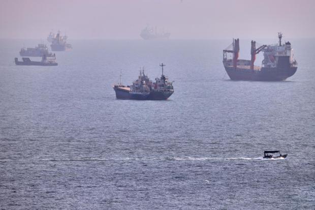 A small boat sails past cargo ships and other vessels anchored in the Strait of Hormuz.