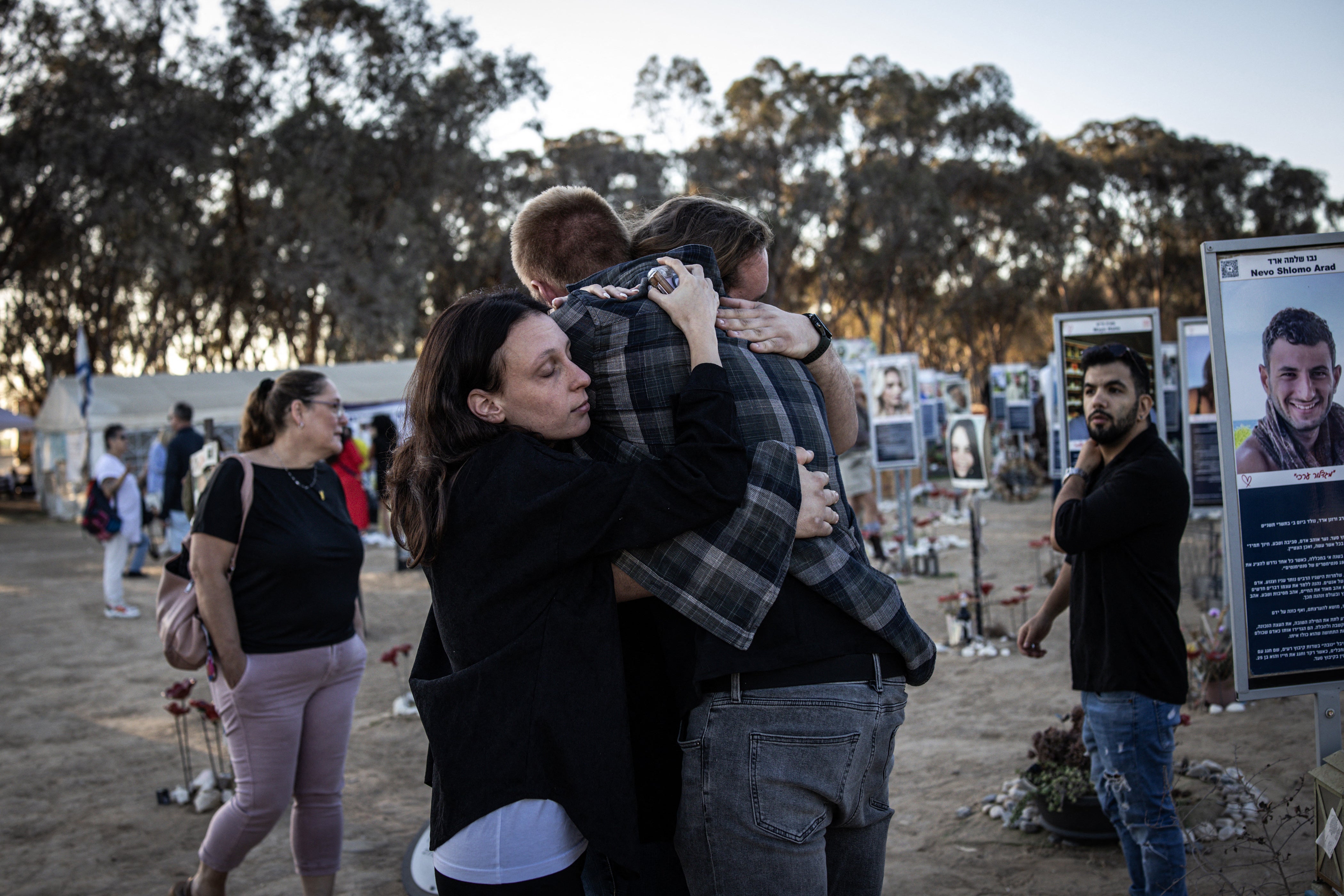 People embrace next to memorials of victims of the 2023 October 7 attacks at the Nova Festival grounds in Reim