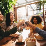 A group of friends is toasting together during a dinner party. They are smiling, celebrating together.