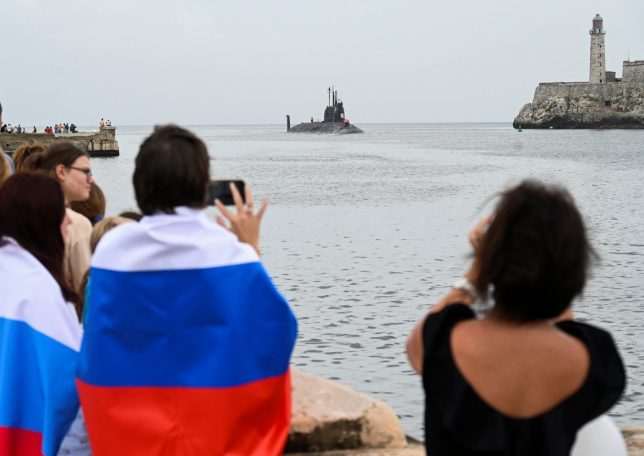 People with Russian flags look at the Russian nuclear-powered submarine Kazan, part of the Russian naval detachment visiting Cuba, arriving at Havana's harbour, June 12, 2024. The Russian nuclear-powered submarine Kazan -- which will not be carrying nuclear weapons -- and three other Russian naval vessels, will dock in the Cuban capital from June 12-17. The unusual deployment of the Russian military so close to the United States -- particularly the powerful submarine -- comes amid major tensions over the war in Ukraine, where the Western-backed government is fighting a Russian invasion. (Photo by YAMIL LAGE / AFP) (Photo by YAMIL LAGE/AFP via Getty Images)