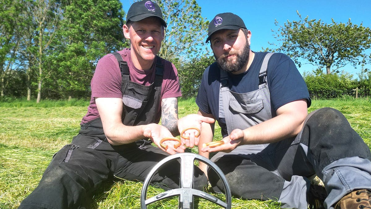 Two metal detectorists holding three Bronze Age gold bracelets