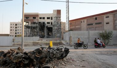Men on motorbikes drive past cars and a residential building damaged in a March 8 U.S.-Israeli strike in Tehran, Iran.