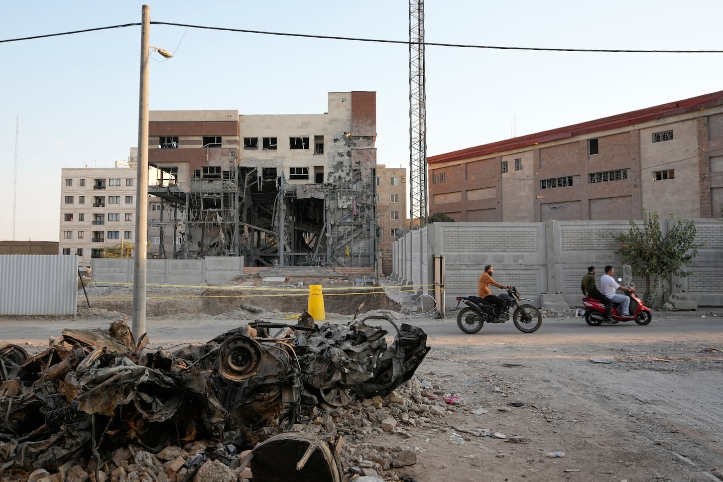Men on motorbikes drive past cars and a residential building damaged in a March 8 U.S.-Israeli strike in Tehran, Iran.