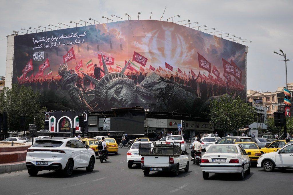 A billboard depicting a fallen Statue of Liberty and crowds carrying Iranian and Shiite flags overlooks Revolution Square as traffic drives by in Tehran, Iran.