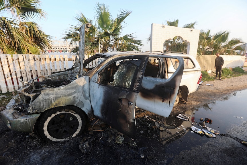 A boy looks at the wreckage of a small white car damaged in an air strike.