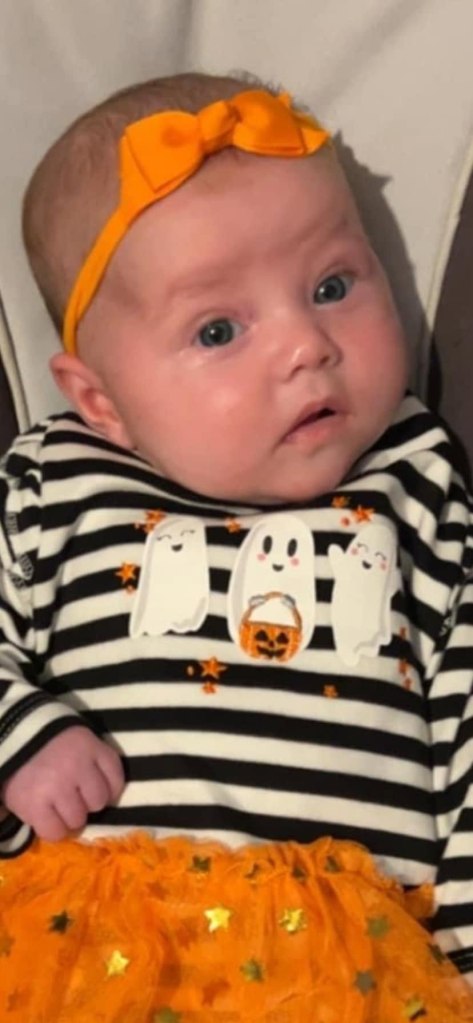 Three-month-old Dahlia-Rose in a black and white striped shirt with ghost decorations and an orange tutu.