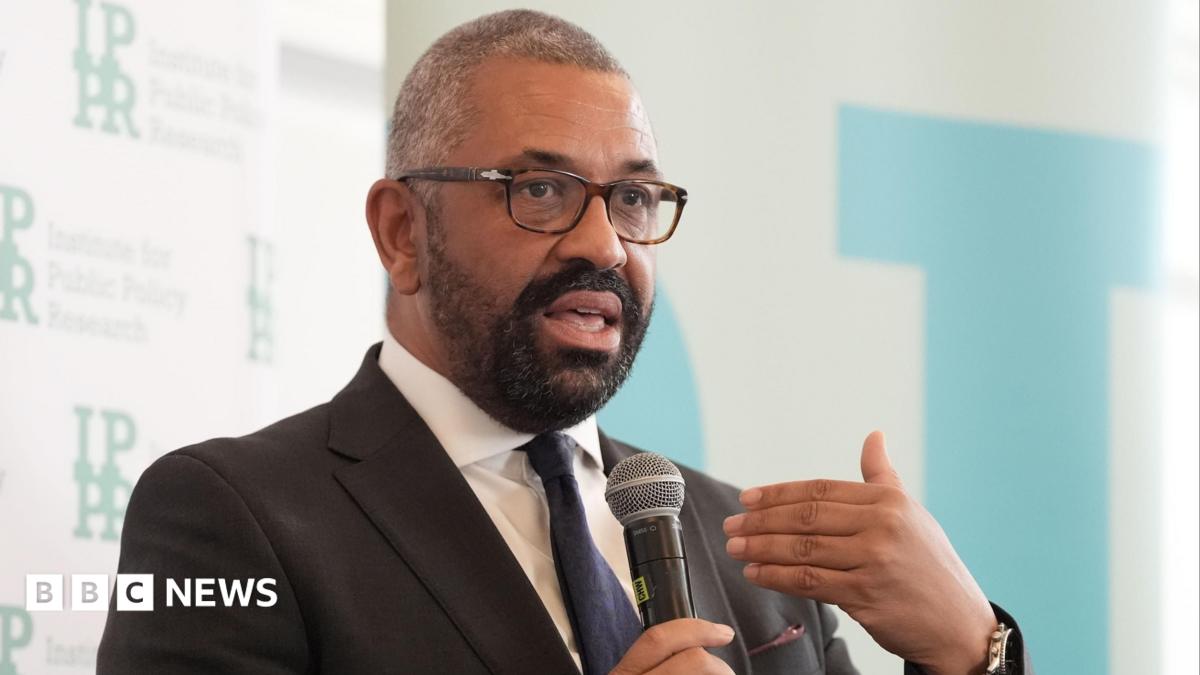 James Cleverly wears a suit and holds a microphone