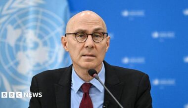 Volker Türk wearing a dark suit and red tie. He is speaking into a microphone.