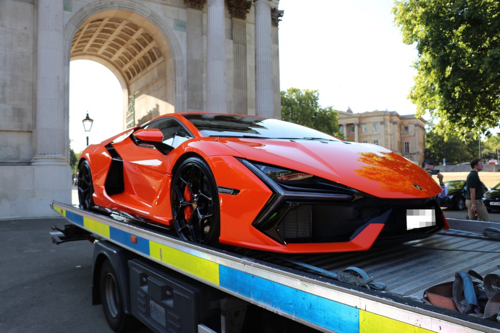 Bright orange Lamborghini parked on a tow truck with a historic building in the background. Bright orange Lamborghini parked on a tow truck with a historic building in the background.