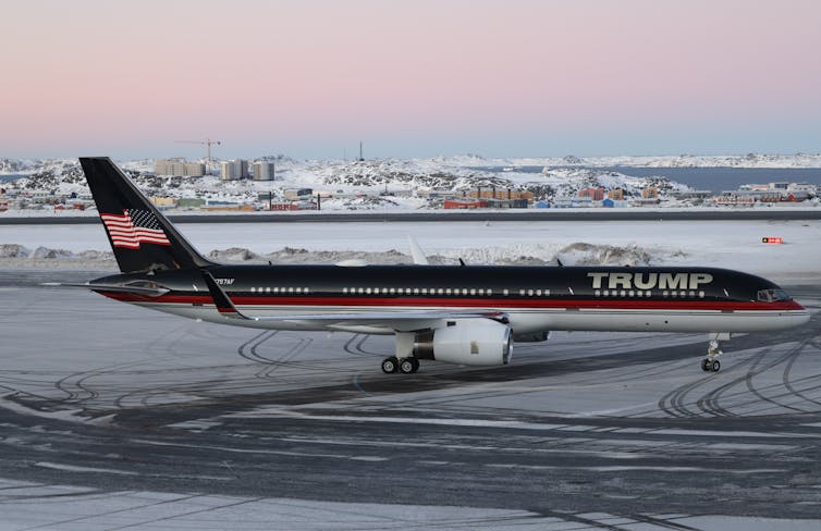 A passenger jet that says Trump on its fuselage sits on a wintry runway.
