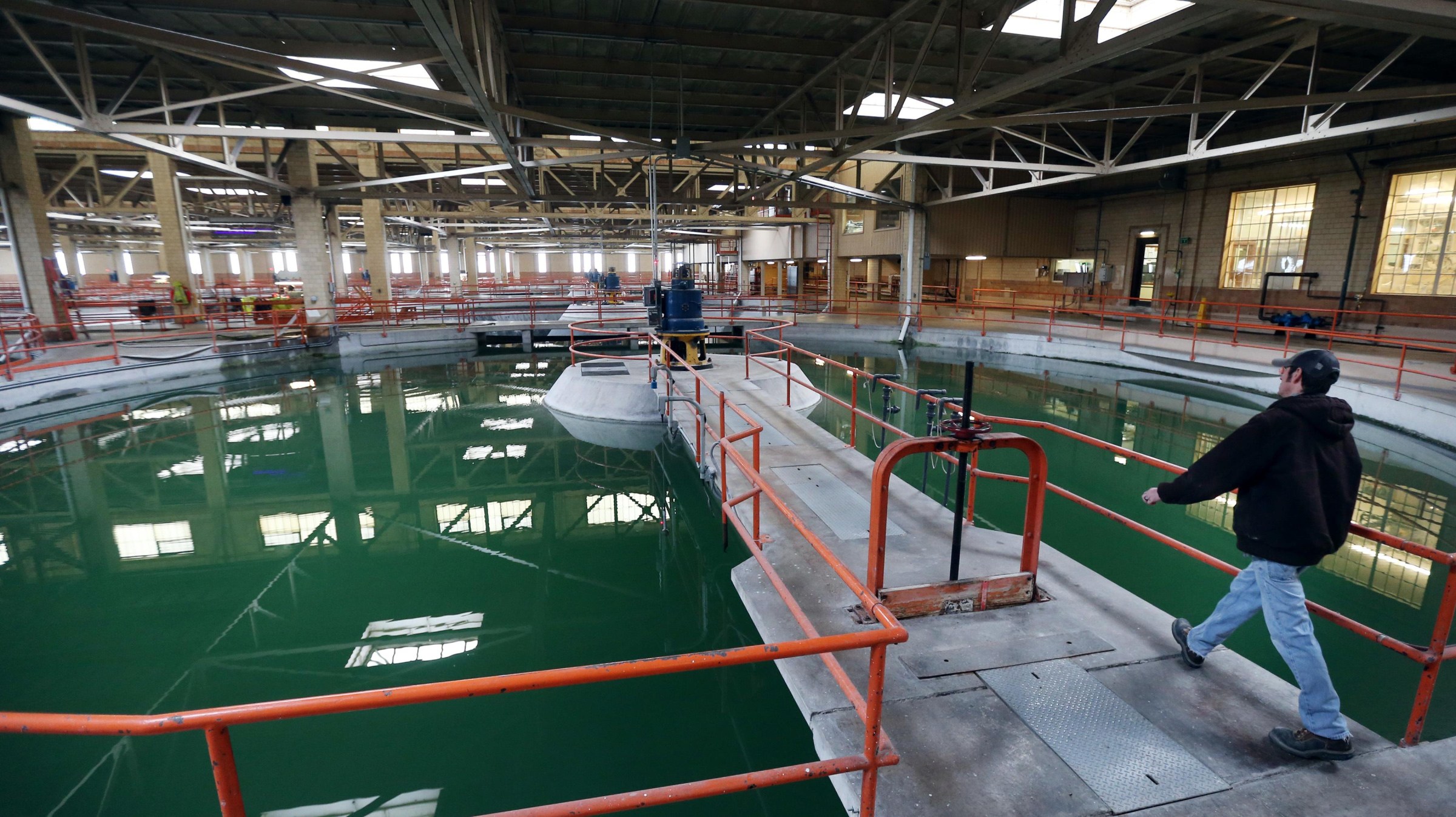 Workers on walkways over green lagoons in an indoor water treatment plant.