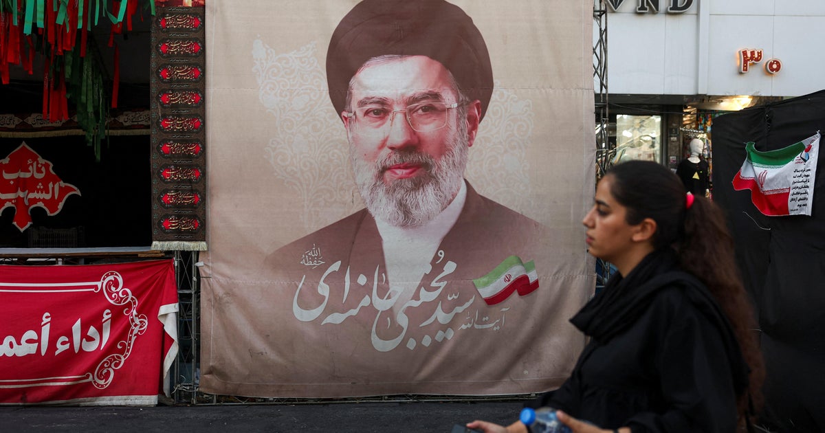 A woman walks next to a banner with a picture of Iran's Supreme Leader Mojtaba Khamenei in Tehran